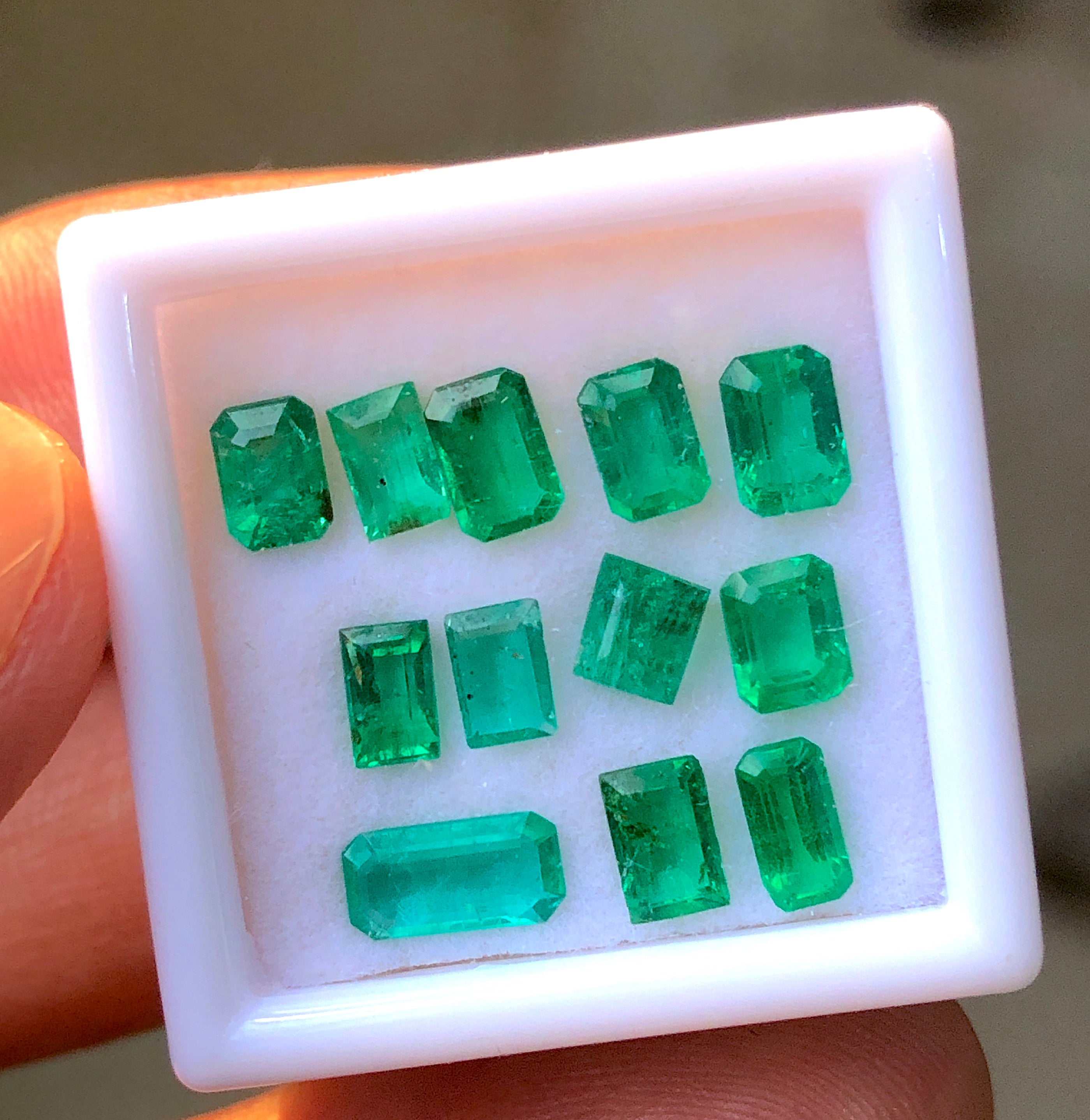 Box of emerald gemstones held by a hand